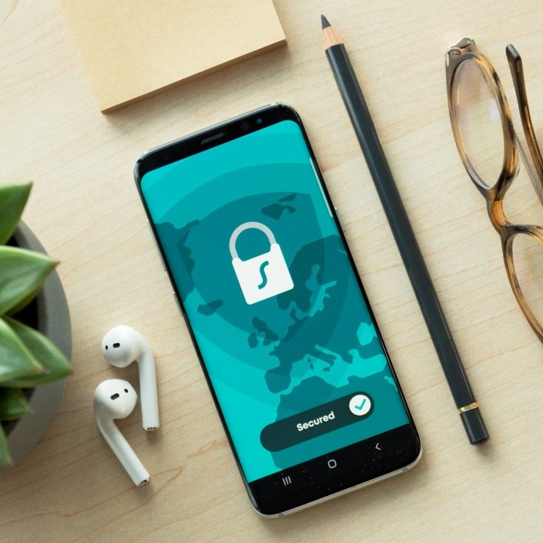 Datenschutz Smartphone mit Sperrsymbol auf einem Tisch, umgeben von Pflanzen, Brille und Stift.